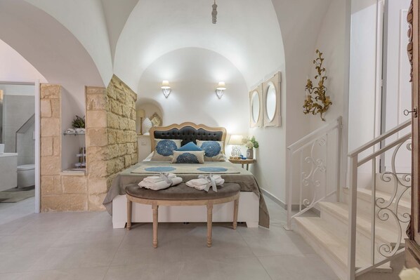 A bedroom with a bed, a bench with towels, stone walls, and a staircase.