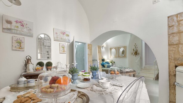 A dining area with a table set for a meal, surrounded by potted plants and artwork. - 2666 La Maisonnette - Appartamento 1 (Nardò)