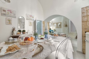 A dining area with a table set for a meal, surrounded by potted plants and artwork.