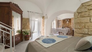 A bedroom with a large bed, a wooden wardrobe, a mirror, a potted plant, and a stone wall. - 2666 La Maisonnette - Appartamento 1 (Nardò)