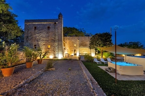 A stone building with a swimming pool, outdoor seating, and potted plants.