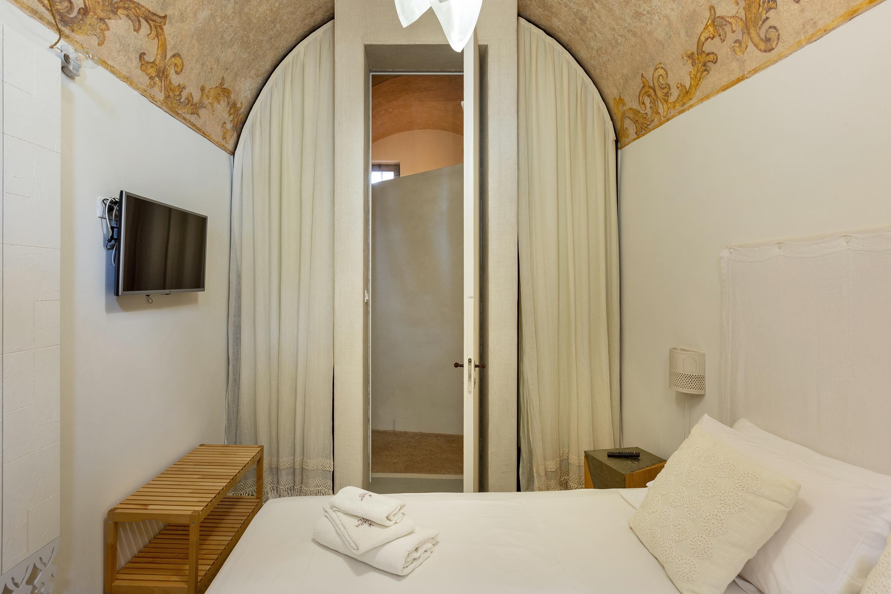 Une chambre d’hôtel avec un lit, un banc en bois, un téléviseur fixé au mur et une porte donnant sur un balcon.