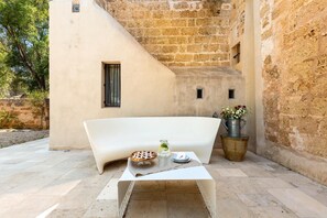 A modern outdoor seating area with a white sofa, a small table with a pie, a pitcher of lemonade, and a flower pot.
