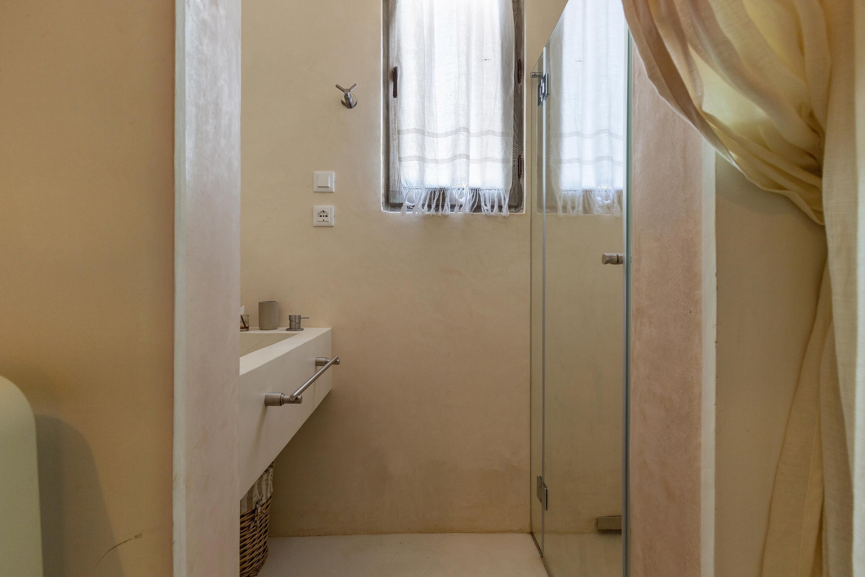 A small bathroom with a shower, a sink, and a window with curtains.