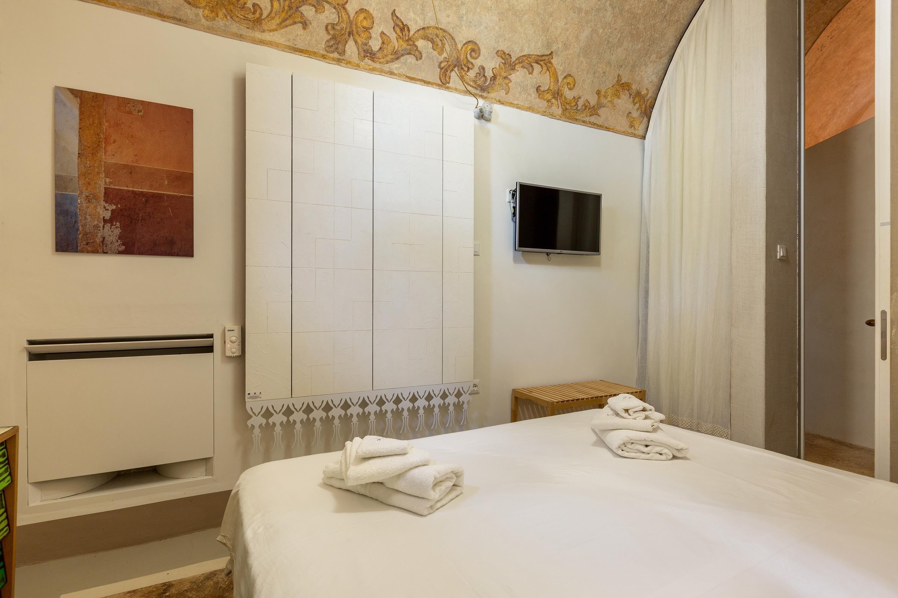 Ein Hotelzimmer mit einem Bett, einem flachbildfernseher an der Wand, einer Heizung und einem kleinen Holzschemel.