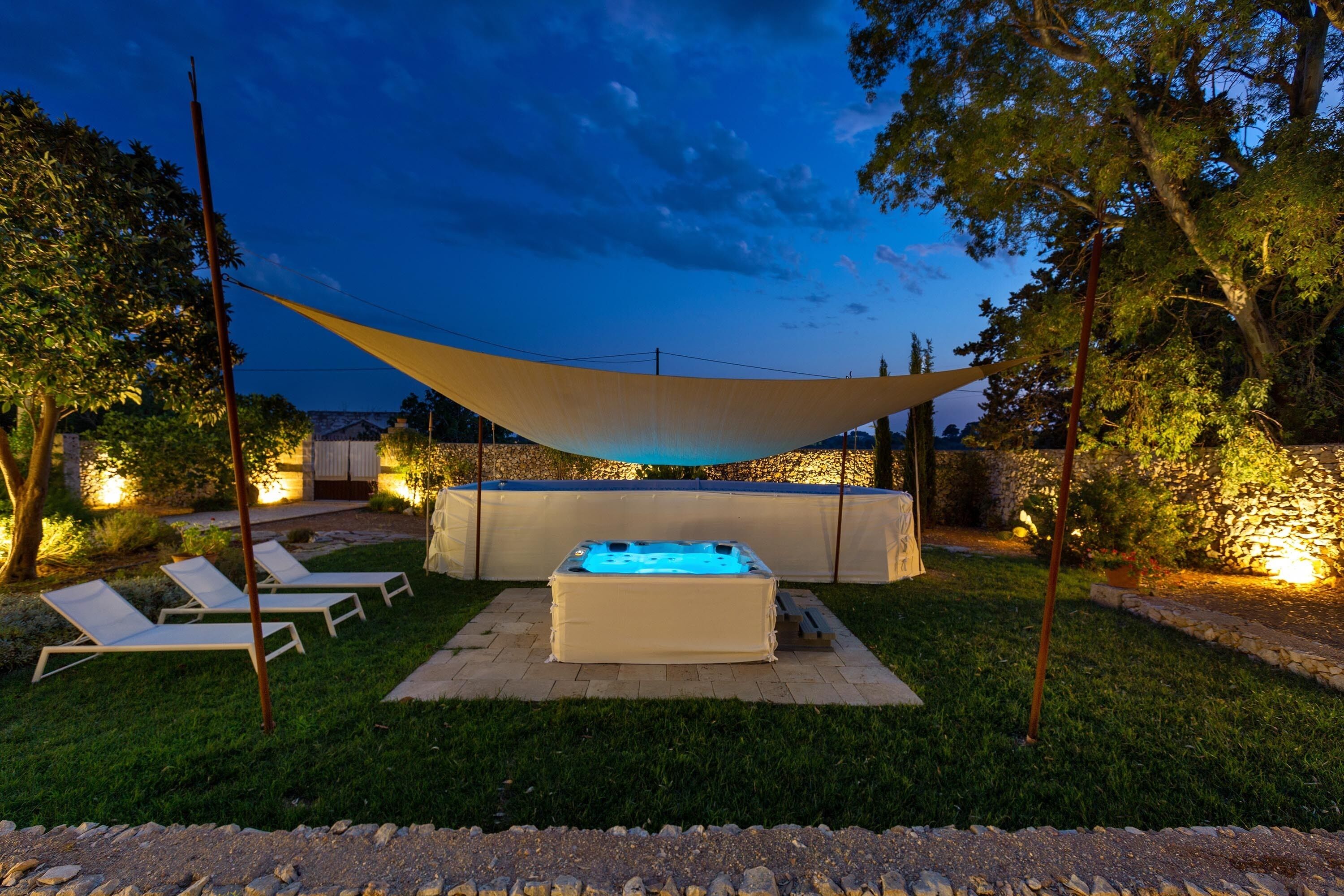 Una vasca idromassaggio in un giardino con sedie a sdraio e un gazebo.