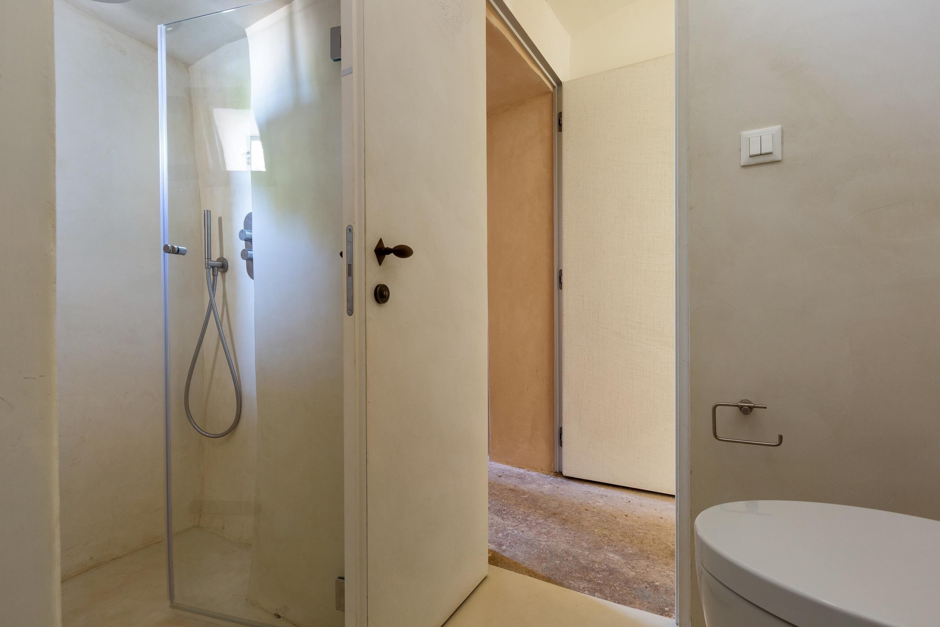 A bathroom with a toilet, a shower enclosure, and a door leading to another room.