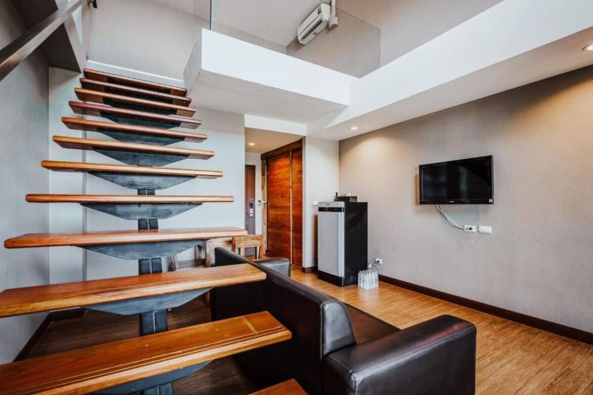 A modern interior with a spiral staircase, a flat-screen TV mounted on the wall, and a seating area with wooden tables and black leather chairs.