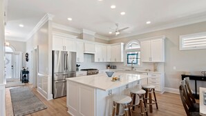 A modern kitchen with white cabinetry, stainless steel appliances, a central island with stools, and a ceiling fan.
