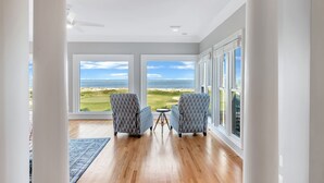A room with large windows, two patterned chairs, a small table, and a wooden floor.