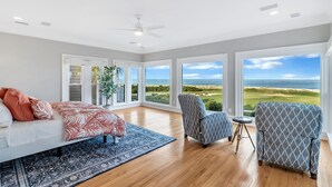 A spacious room with a large bed, two armchairs, and a view of a golf course and ocean.
