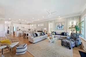 A spacious living area with a sofa, ottoman, and coffee table, a dining area with chairs, and a kitchen in the background.