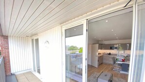 Un apartamento moderno con un ventanal corredero que da a un balcón, una cocina con electrodomésticos contemporáneos y un pequeño rincón de estar.
