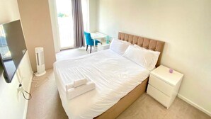 Habitación de hotel con una cama grande, un escritorio, una silla, un televisor y una ventana con cortinas.