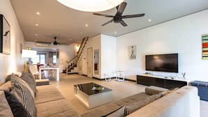 Una sala de estar moderna con un televisor de pantalla plana grande, un ventilador de techo y una escalera que conduce a un piso superior.