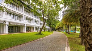 Un camino bordeado de árboles y un edificio con varios balcones.