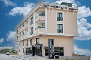 Un edificio de varios pisos con balcones, un cartel que dice 'Luxury Airport Hotel' y un número de contacto.