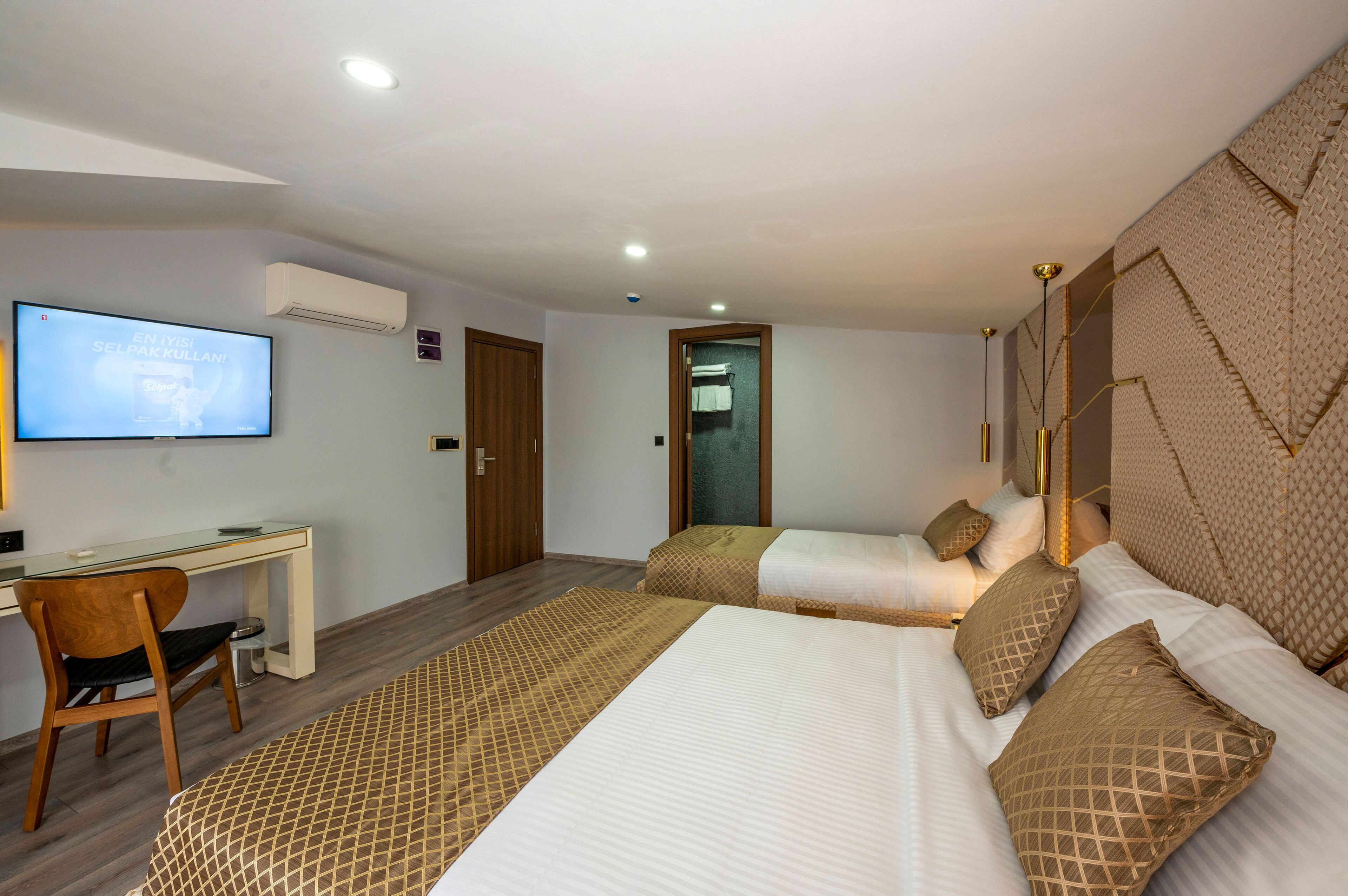 Habitación de hotel con dos camas, un escritorio, un televisor y una puerta que da a un baño.
