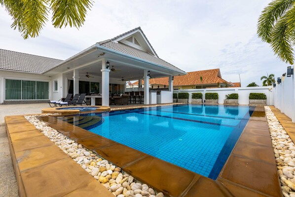 A swimming pool with a covered patio area, a tiled deck, and a white building with a tiled roof. - Private 3 Bedroom Pool Villa PP10 (Hua Hin)