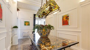 Ein Essbereich mit einem Tisch mit Glasplatte, einer verzierten Metalllüster und einer großen, dekorativen Vase mit Blumen.