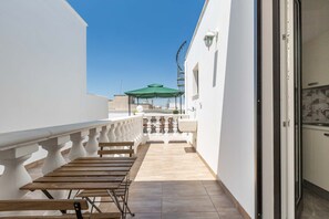 A balcony with a wooden table and chairs, a green umbrella, and a view of the cityscape. - 2446 Palazzo Montagna - Mono by Barbarhouse (Melissano)