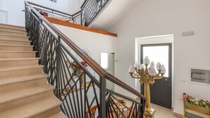 Eine Treppe mit einem Holzgeländer und schwarzen Metallreling, die zu einer Empore mit einem Chandelier und einer Tür führt.
