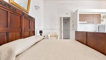 Una camera da letto con un letto grande, una testiera in legno, una sedia e vista sulla cucina adiacente.
