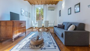 A living room with a wooden ceiling, a grey sofa, a wooden cabinet, a dining table with chairs, and a patterned rug.