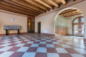 A spacious hall with a checkered floor, wooden ceiling beams, and a large arched doorway. - GuestHost - Palazzo Manfredini Exclusive & Deluxe Apartment (Ferrara)