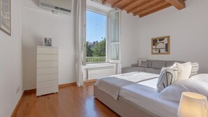 A bedroom with a bed, a dresser, a window, a radiator, and a ceiling with wooden beams.