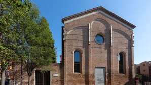 A brick building with arched windows and a door, surrounded by trees and a clear sky.