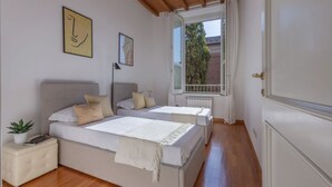 A bedroom with two beds, a radiator, a window with curtains, and a plant on a nightstand.