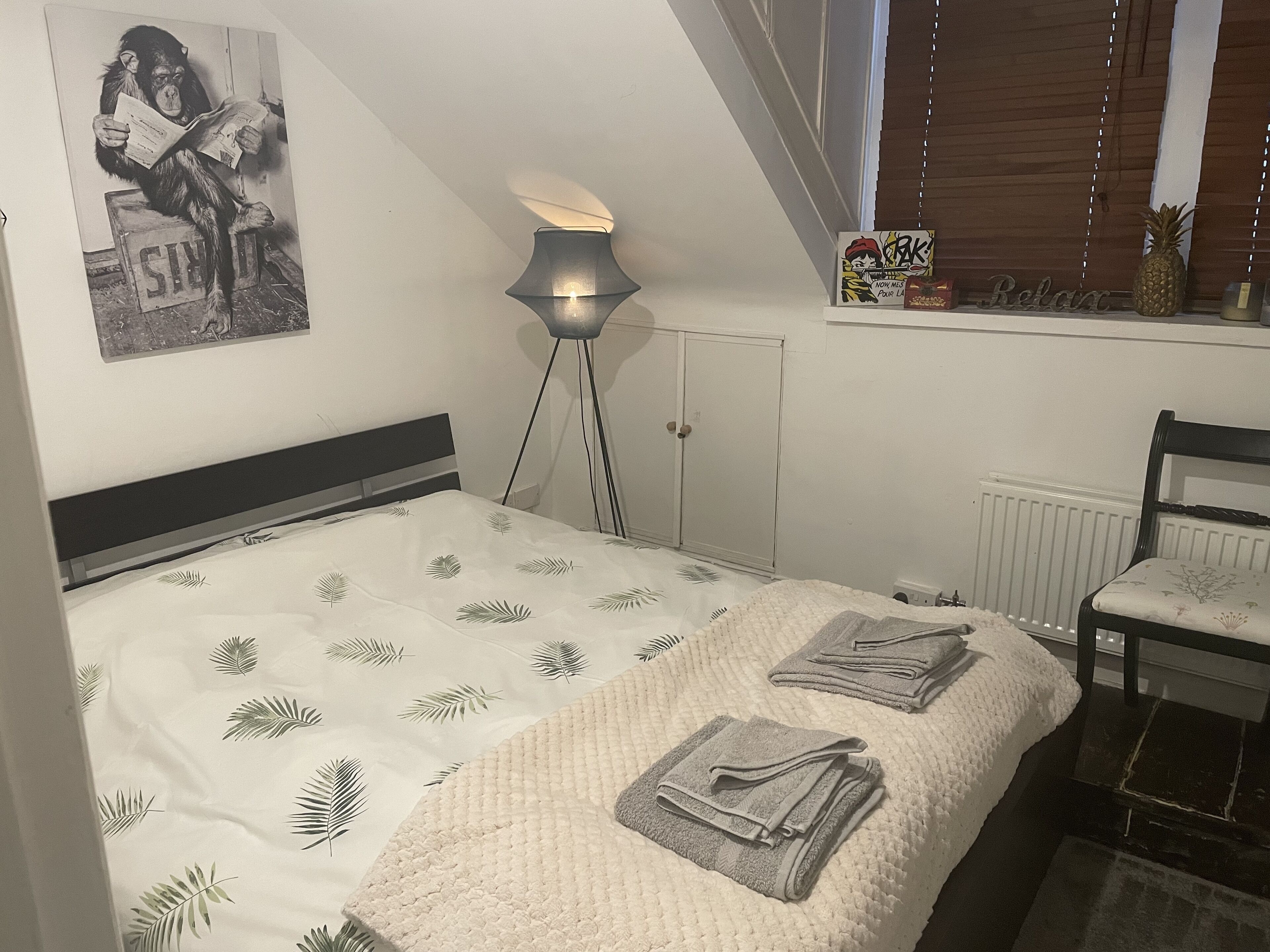 A bedroom with a bed, a floor lamp, a radiator, a window with blinds, a chair, and a poster on the wall.