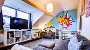 A cozy living room with a flat-screen TV, a bookshelf, a sofa, and a vibrant mural on the wall. - Entire Artistic Open-plan Top Floor Apartment (Westcliff-on-Sea)