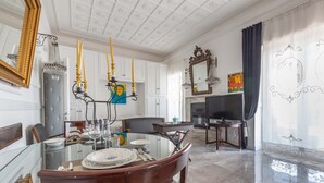 A dining area with a glass table, chairs, and a chandelier. There is a television and a fireplace in the background. - 2448 Palazzo Montagna - Suite by Barbarhouse (Melissano)