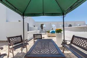A terrace with a table and benches under a green canopy, overlooking a white building with arches. - 2448 Palazzo Montagna - Suite by Barbarhouse (Melissano)