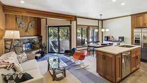 A modern kitchen with a central island, wooden cabinets, and a stone fireplace. - One Bedroom walking distance to Palisades Tahoe! (Olympic Valley)