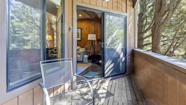 A wooden deck with a glass door leading to a room with a sofa, lamp, and a framed picture. - One Bedroom walking distance to Palisades Tahoe! (Olympic Valley)