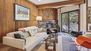 A living room with a stone fireplace, wooden walls, a sofa, and a coffee table. - One Bedroom walking distance to Palisades Tahoe! (Olympic Valley)
