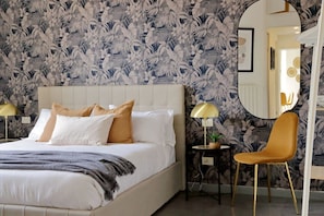 A bed with white bedding and multiple pillows, a small table with a lamp, a chair, and a mirror on the wall.