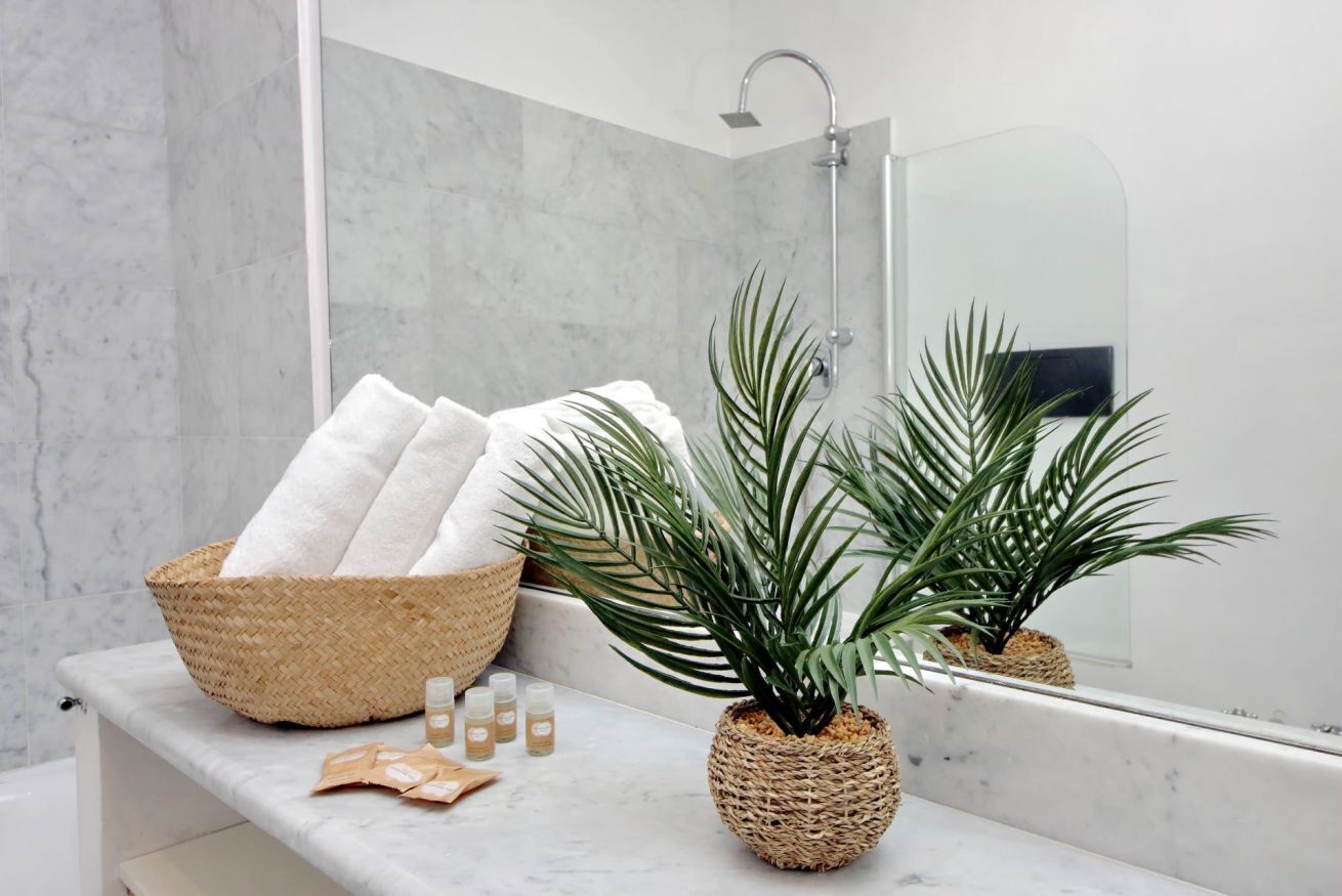 A bathroom with a marble countertop, a woven basket with towels, a potted plant, and a shower.