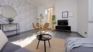 Moderni olohuone, jossa on sohva, ruokapöytä tuoleineen, televisio ja suuri ikkuna.