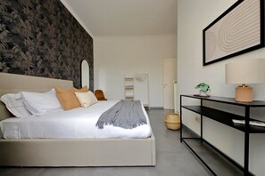 Une chambre à coucher moderne avec un lit, une console, un miroir et un mur orné d’un motif floral.