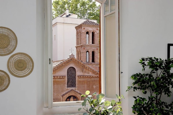 A view through a window to a brick building with a bell tower, a door, and a potted plant.