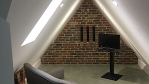 A loft-style room with a sloped ceiling, exposed brick wall, and a flat-screen TV mounted on the wall.