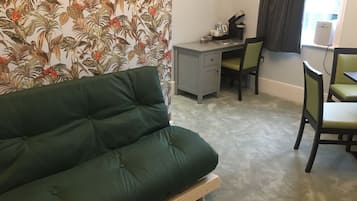 A room with a green sofa, a desk with a chair, and a window with curtains.