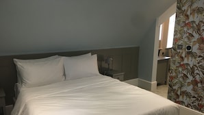 A neatly made bed with white linens, a bedside table with a lamp, and a small drawer.