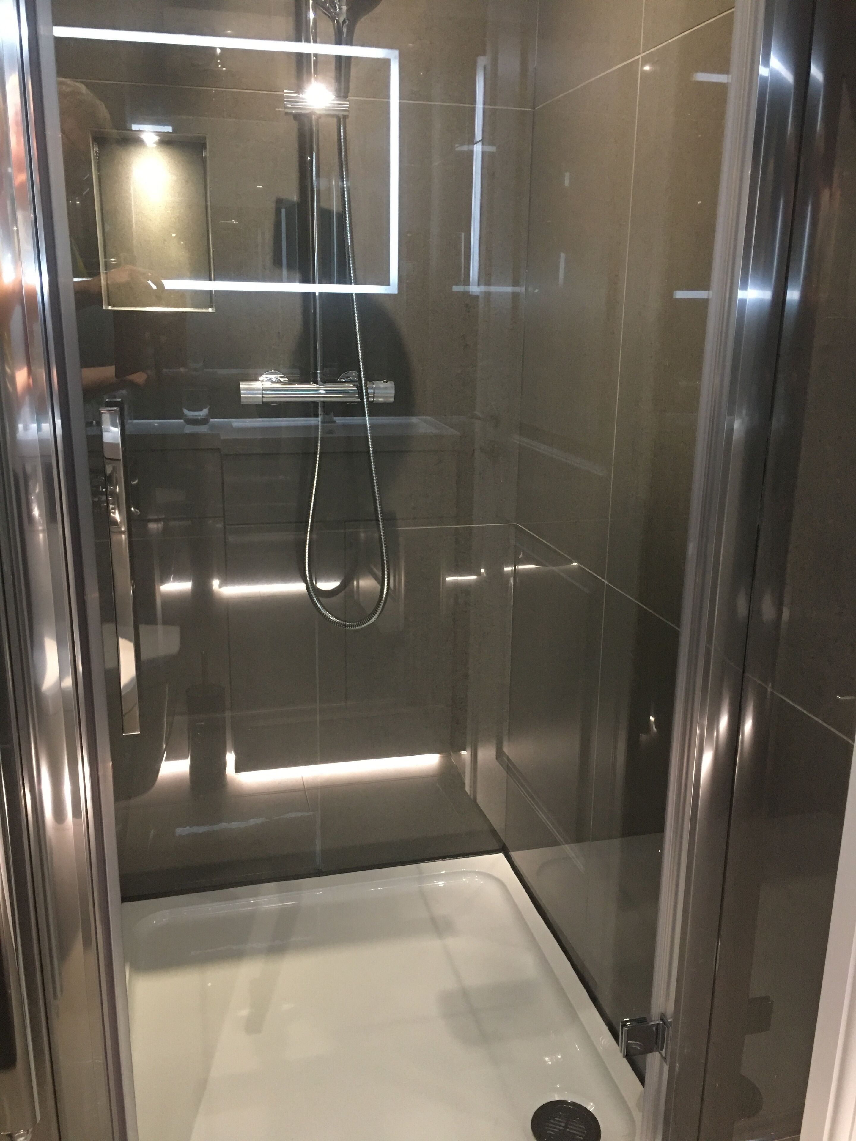 Un box de ducha moderno con puerta de cristal, cabezal de ducha de mano y desagüe visible.