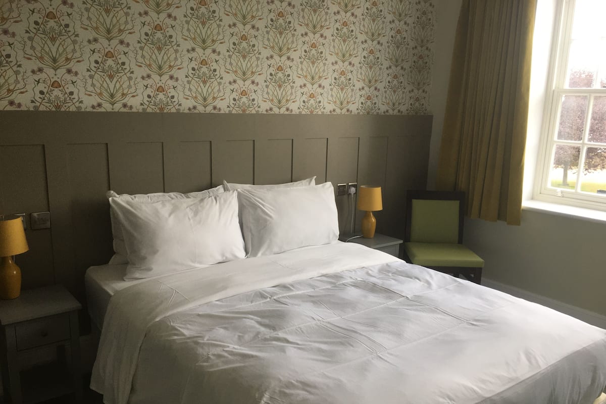 A hotel room with a large bed, two bedside tables with lamps, a chair, and a window with curtains.