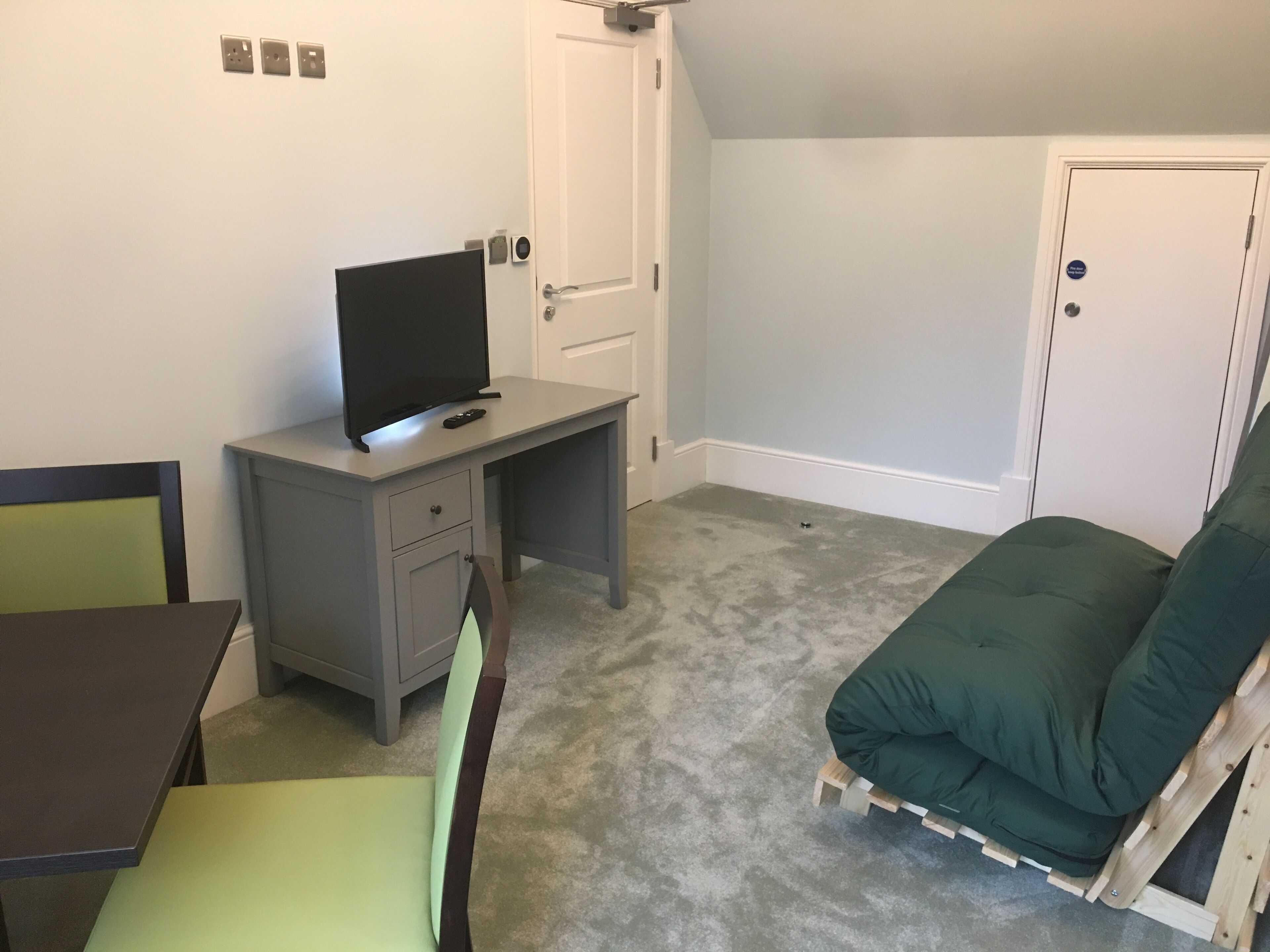 Un dormitorio con una cama, un escritorio con una computadora, una silla y una puerta.